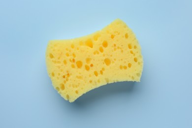 Photo of New yellow sponge on light blue background, top view
