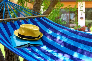 Photo of Comfortable blue hammock with hat and book outdoors on sunny day