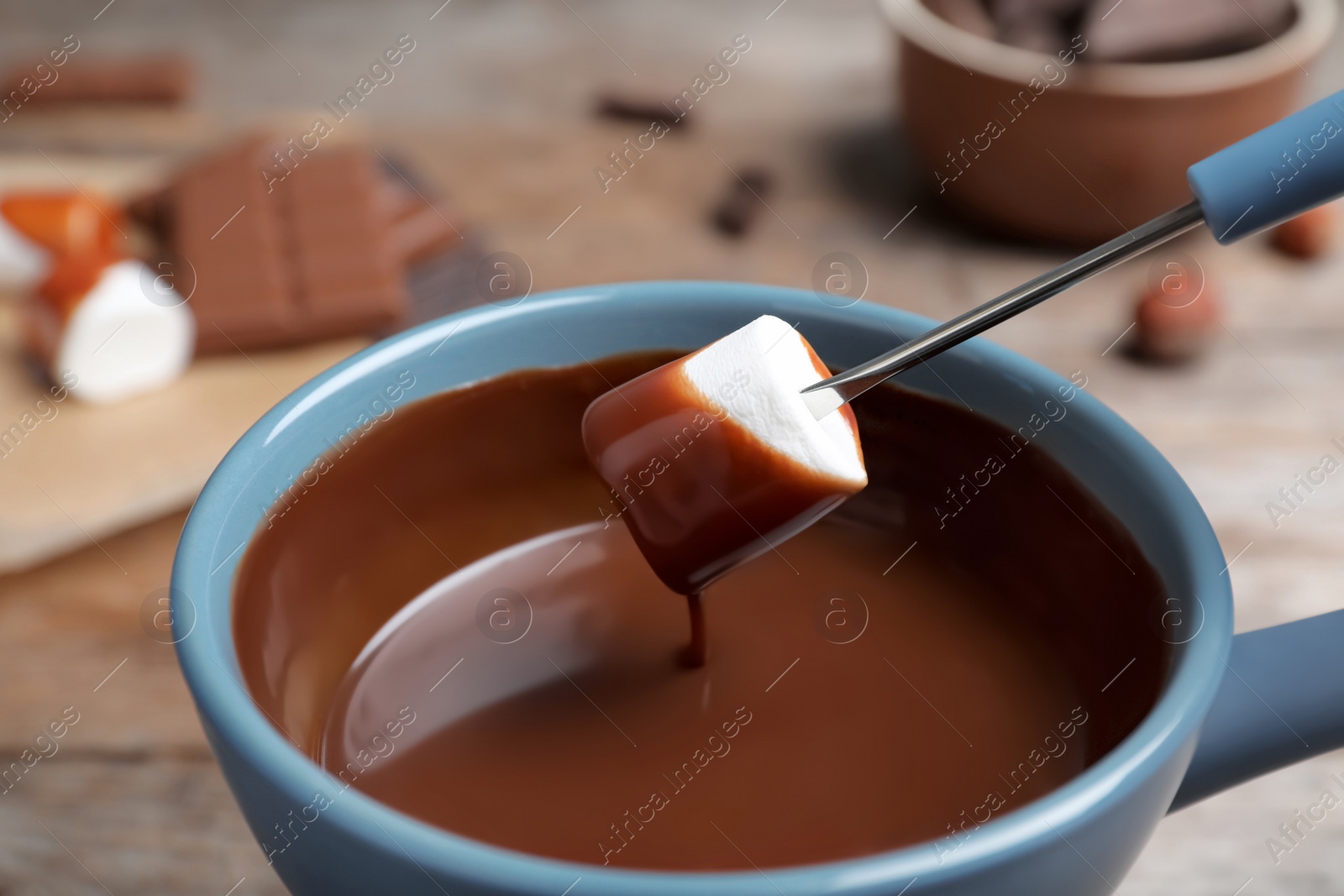 Photo of Dipping marshmallow into pot with chocolate fondue on table, closeup