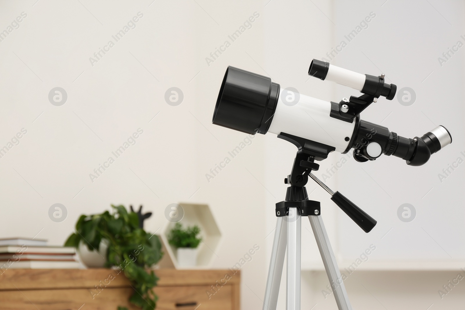 Photo of Tripod with modern telescope in stylish room, closeup. Space for text