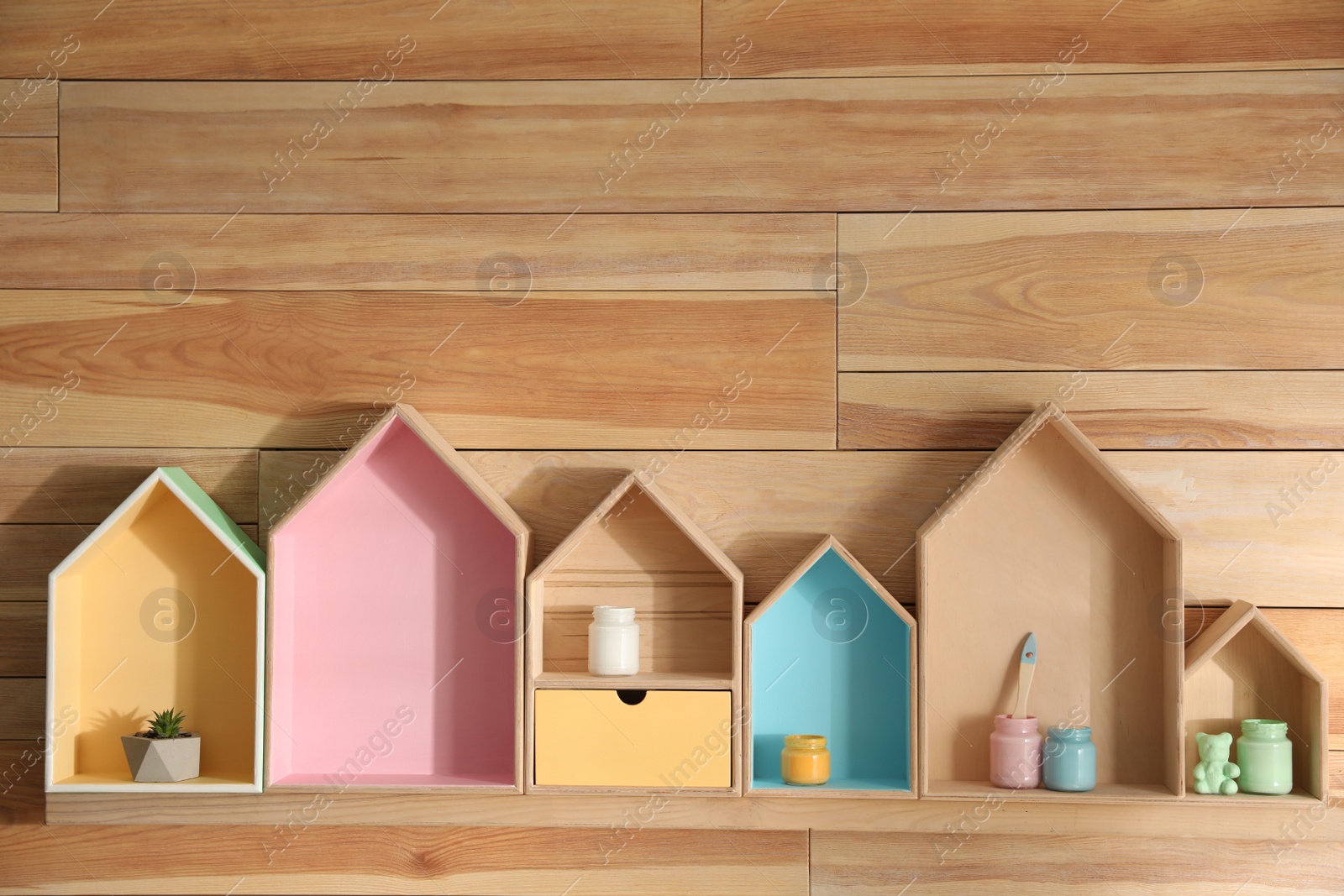 Photo of House shaped shelves with plant and jars of paints on wooden wall, space for text. Interior elements