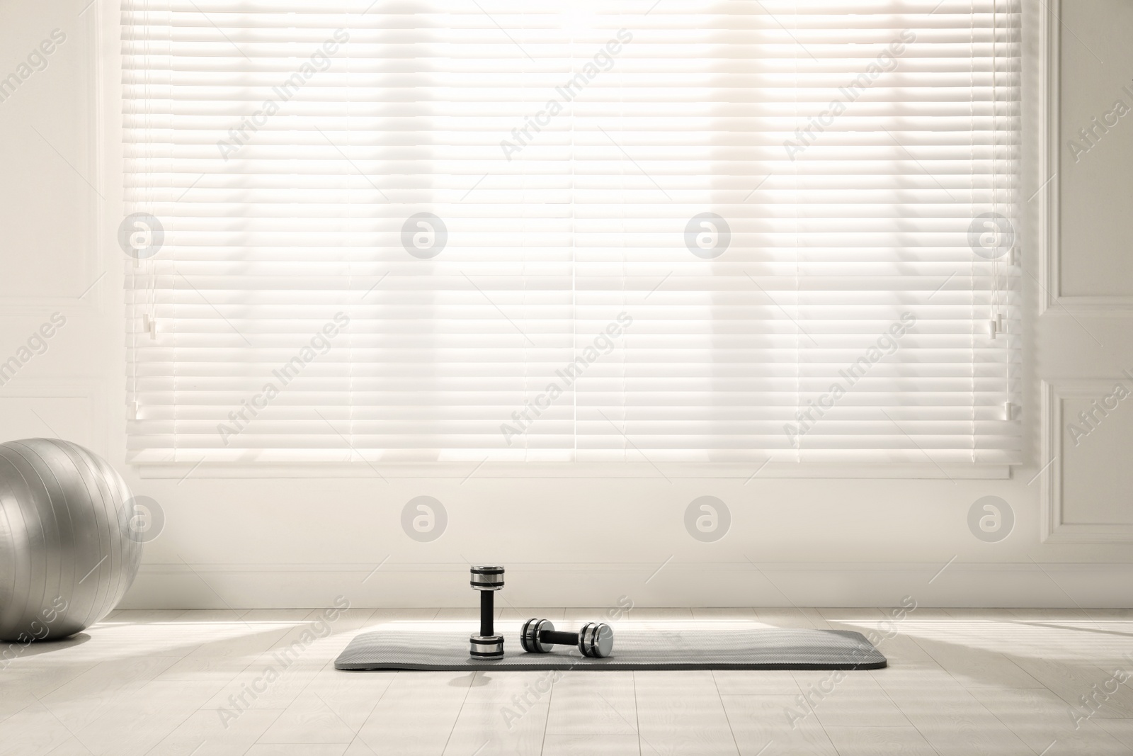 Photo of Mat, dumbbells and fitness ball near window in room