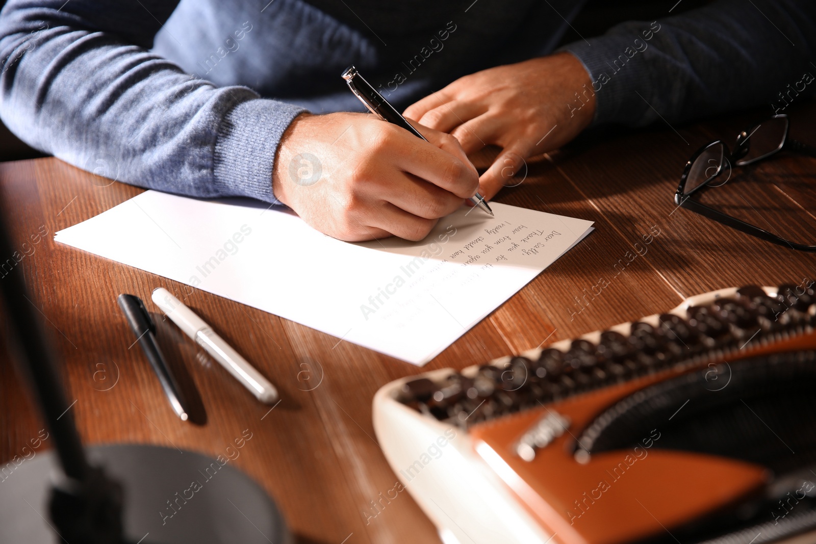 Photo of Man writing letter at wooden table indoors, closeup