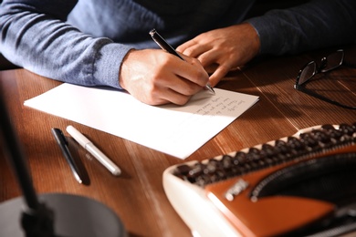 Man writing letter at wooden table indoors, closeup