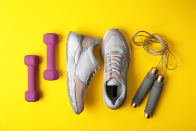 Photo of Flat lay composition of woman's training shoes, dumbbells and jump rope on color background