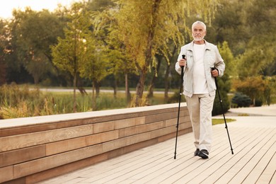 Senior man performing Nordic walking outdoors, space for text