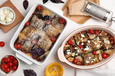 Tasty eggplant rolls in baking dishes on white wooden table, flat lay