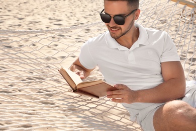 Photo of Young man reading book in hammock on beach