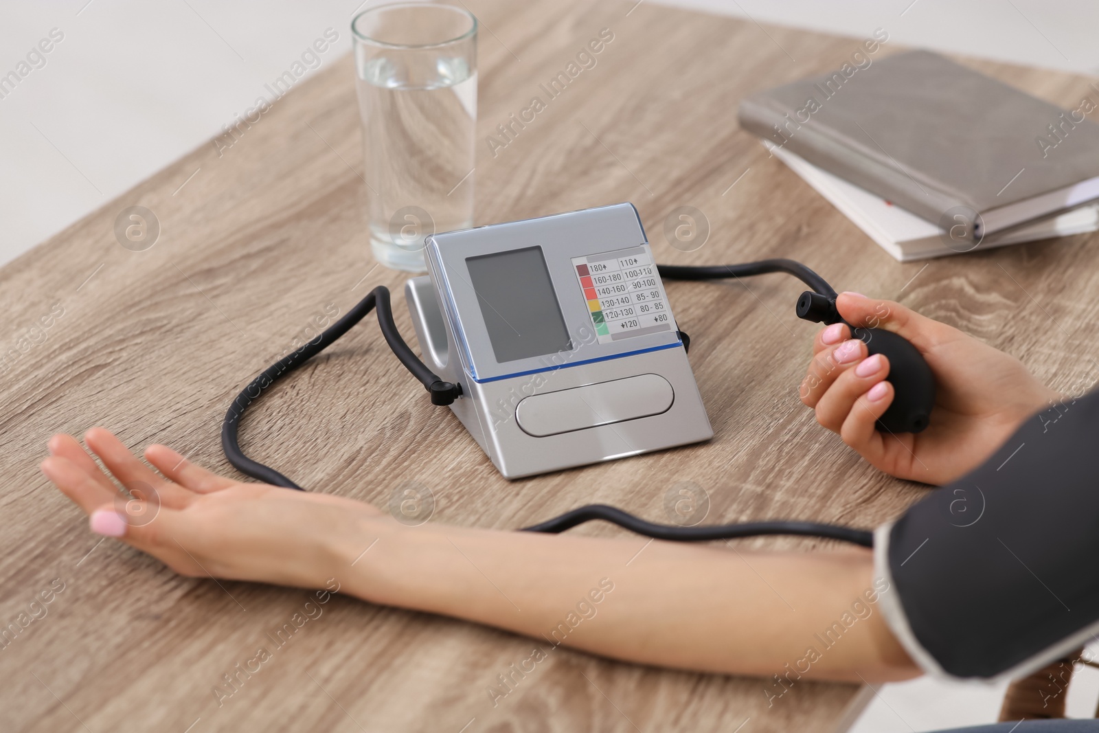 Photo of Woman checking blood pressure at wooden table indoors, closeup