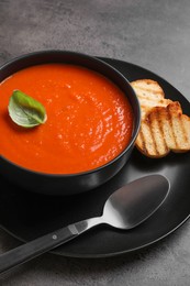 Photo of Delicious tomato cream soup in bowl and pieces of grilled bread served on grey table