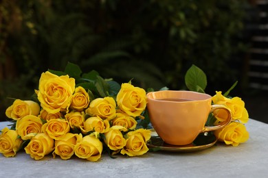 Cup of drink and beautiful yellow roses on light table outdoors, space for text