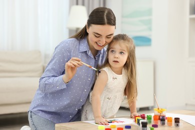 Photo of Mother and her little daughter painting with palms at home