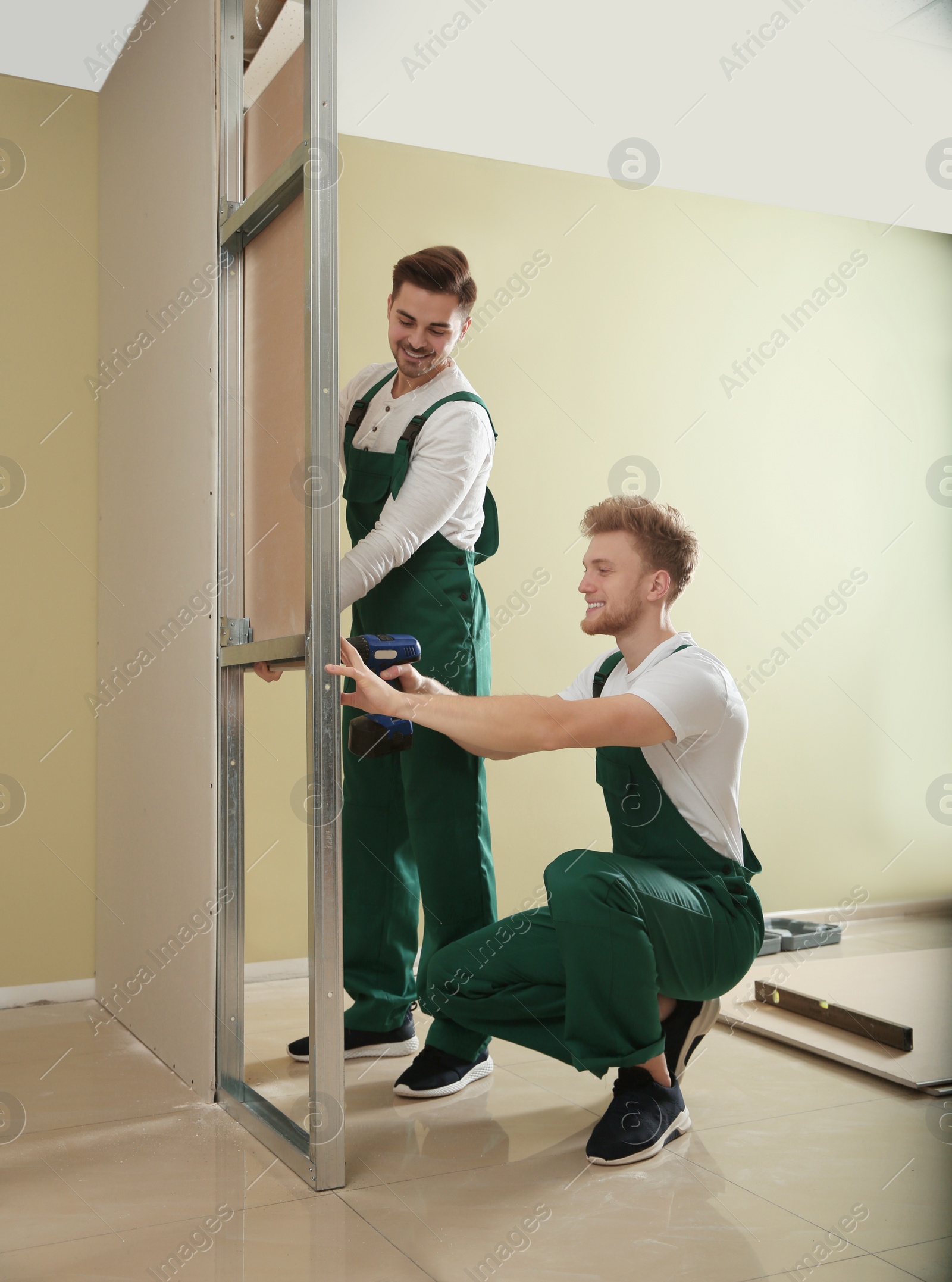 Photo of Young workers installing drywall indoors. Home repair service