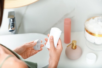 Photo of Woman holding stick deodorant in bathroom, closeup view