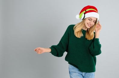 Photo of Happy woman with headphones on grey background, space for text. Christmas music