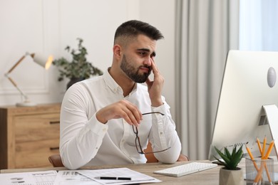 Overwhelmed man with glasses sitting at table in office