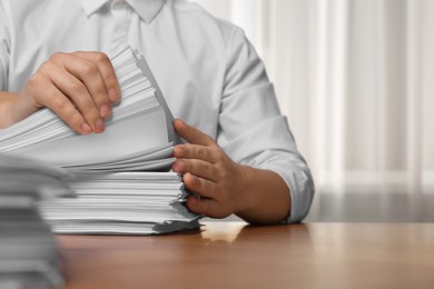 Man stacking documents at table in office, closeup. Space for text