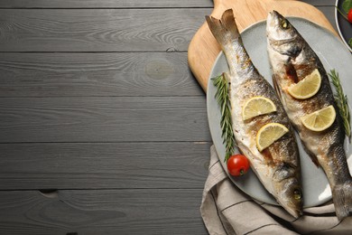 Delicious baked fish, tomato, lemon and rosemary on grey wooden table, top view. Space for text