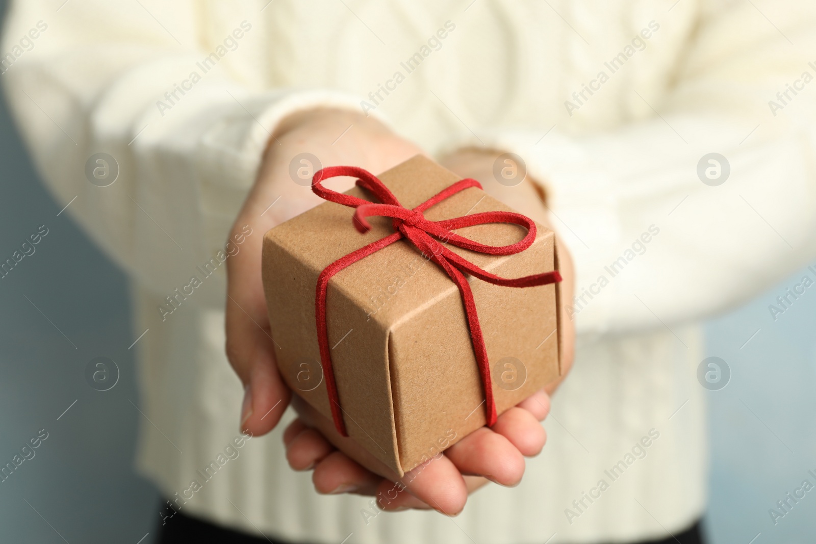 Photo of Woman holding beautiful Christmas gift on light blue background, closeup