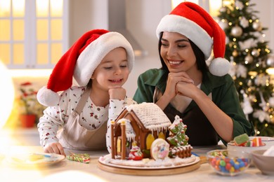 Mother and daughter with gingerbread house at table indoors