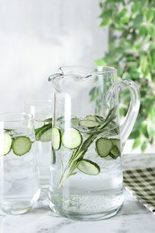 Photo of Refreshing cucumber water with rosemary in jug and glasses on white marble table