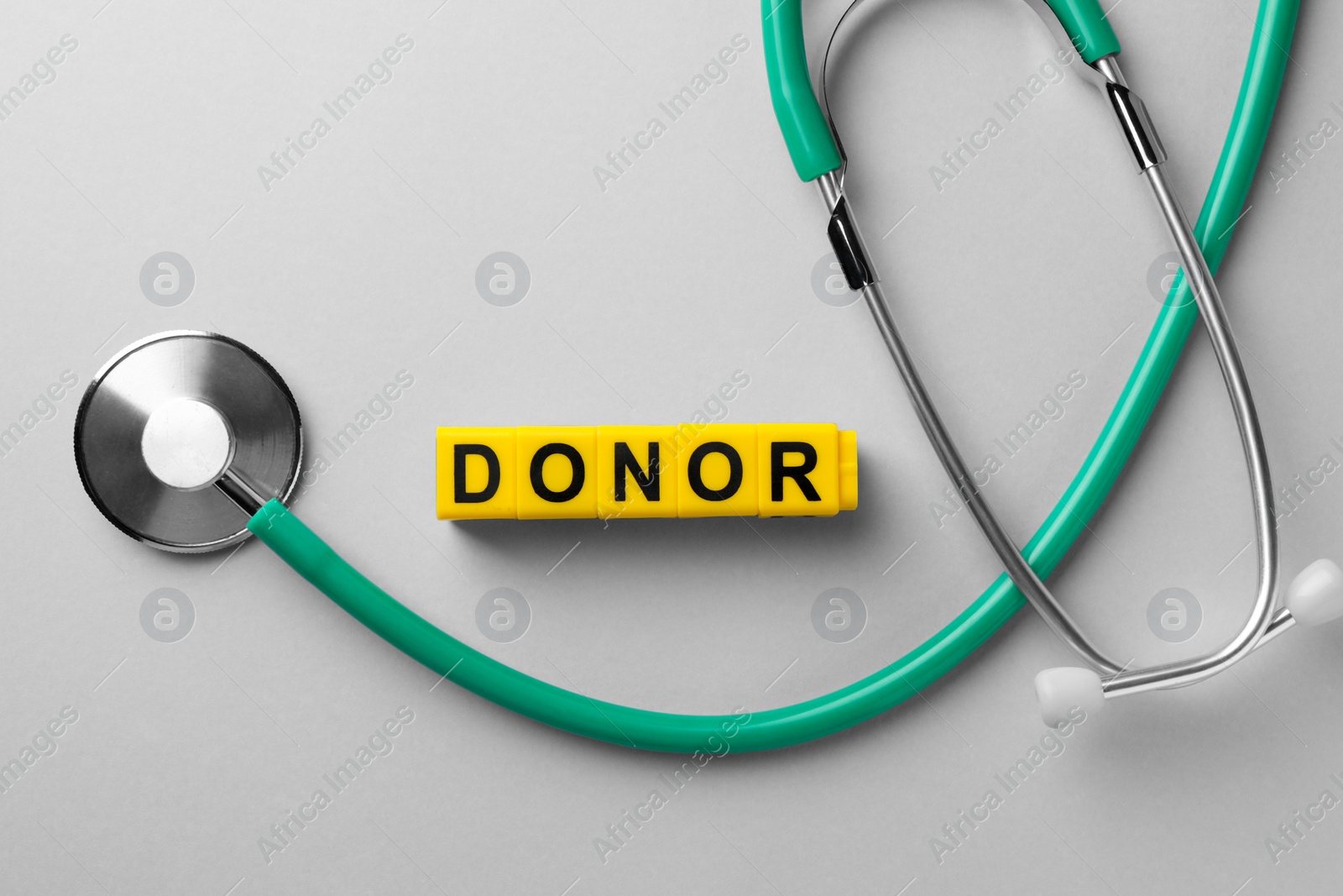 Photo of Word Donor made of cubes and stethoscope on light grey table, flat lay