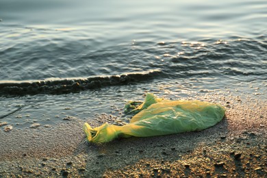 Photo of Used plastic bag near water at beach. Environment pollution