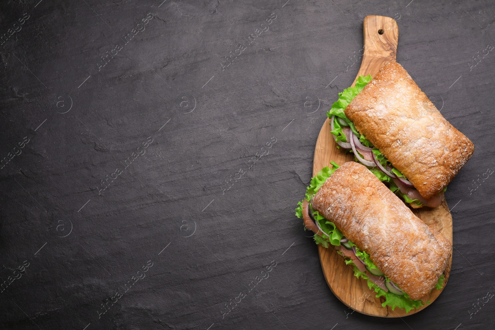 Photo of Delicious sandwiches with fresh vegetables and salmon on black table, flat lay. Space for text