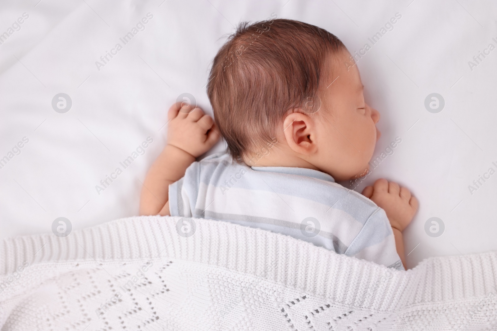 Photo of Cute newborn baby sleeping under plaid in crib, top view