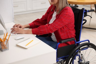 Photo of Woman in wheelchair using computer at table indoors, closeup