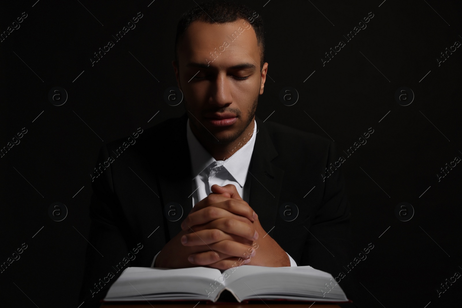 Photo of African American man with Bible praying to God on black background