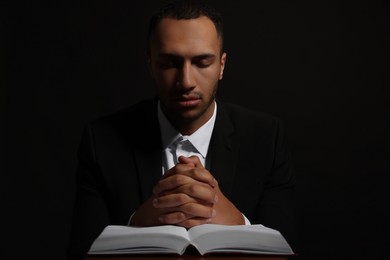 Photo of African American man with Bible praying to God on black background