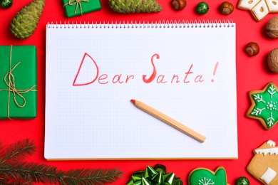 Photo of Notebook with words DEAR SANTA and Christmas decorations on red background, flat lay