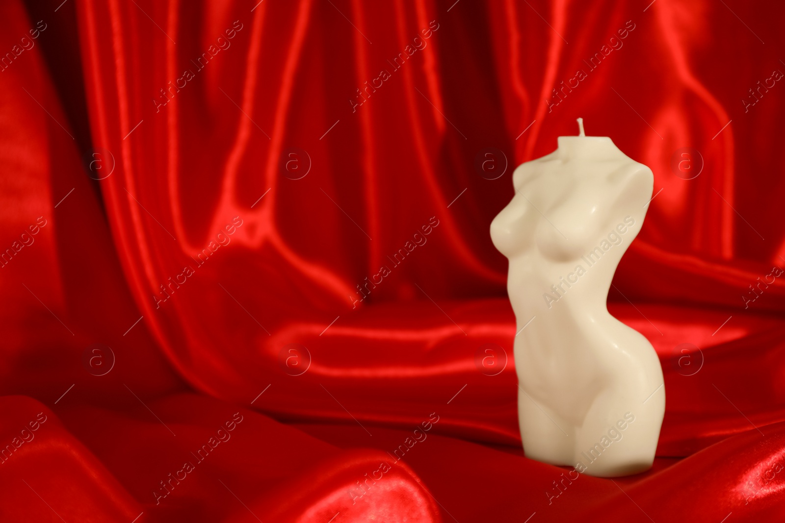 Photo of Beautiful female body shaped candle on red satin. Space for text