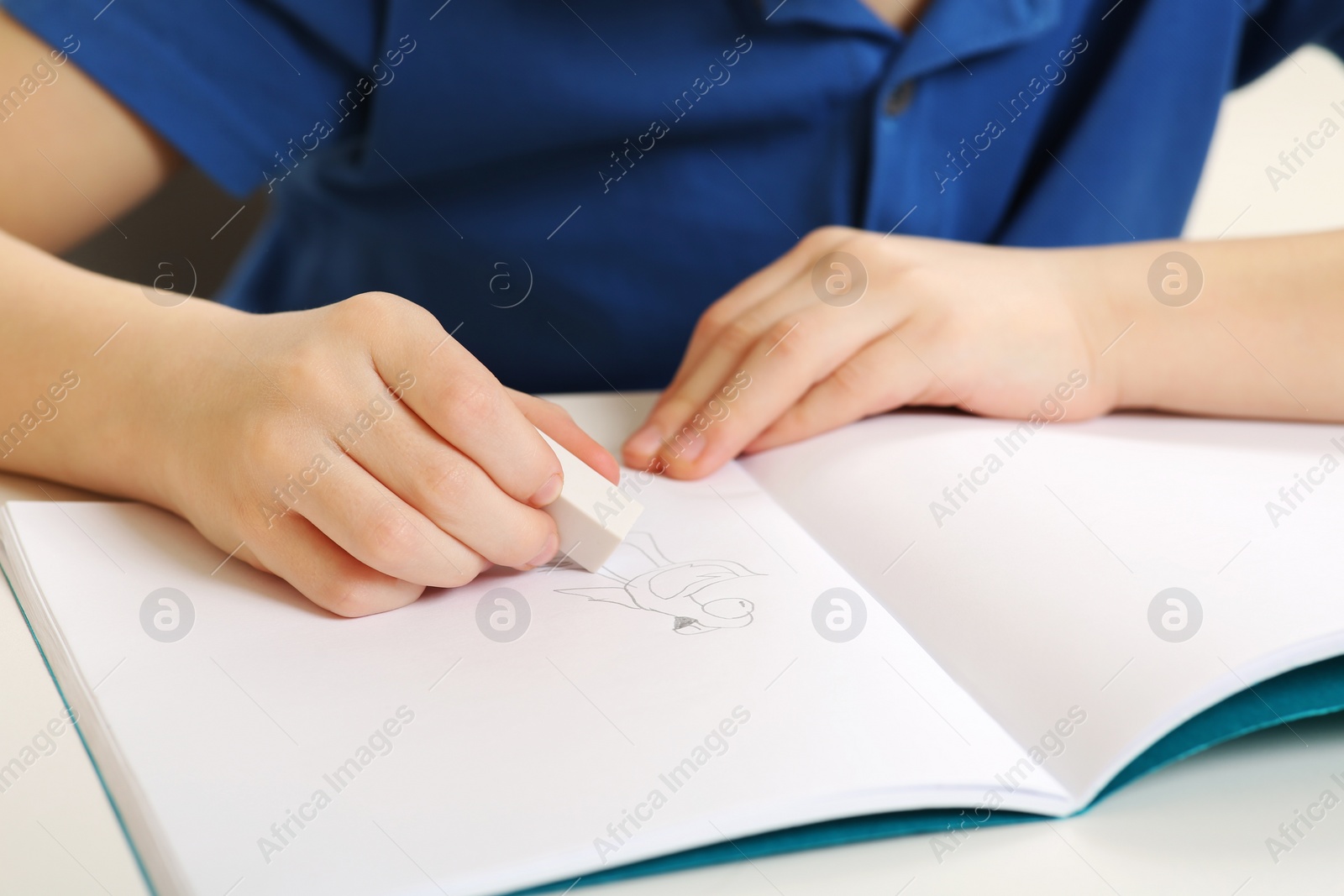 Photo of Boy erasing mistake in his notebook at white desk, closeup