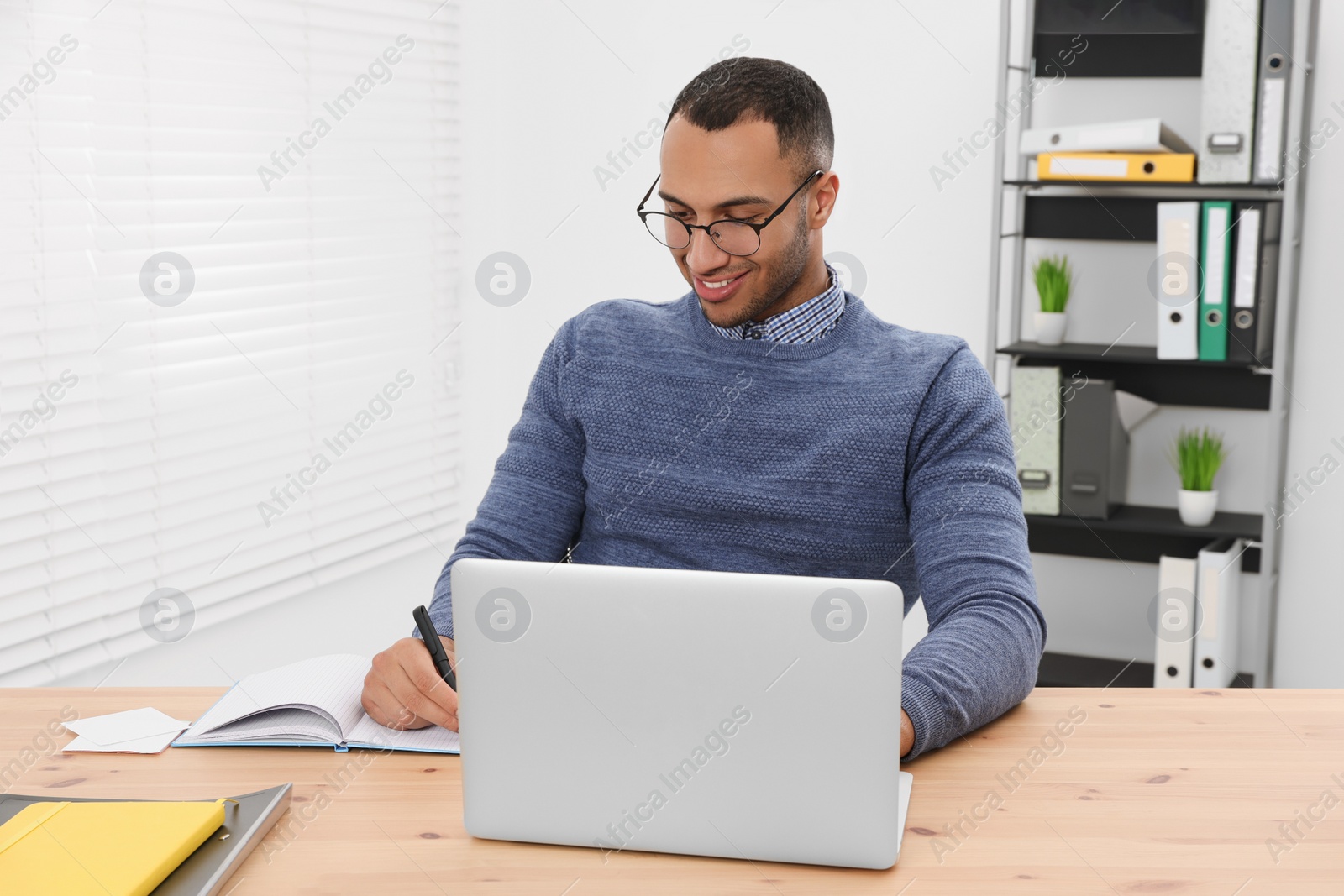 Photo of Happy young intern working with laptop at table in modern office