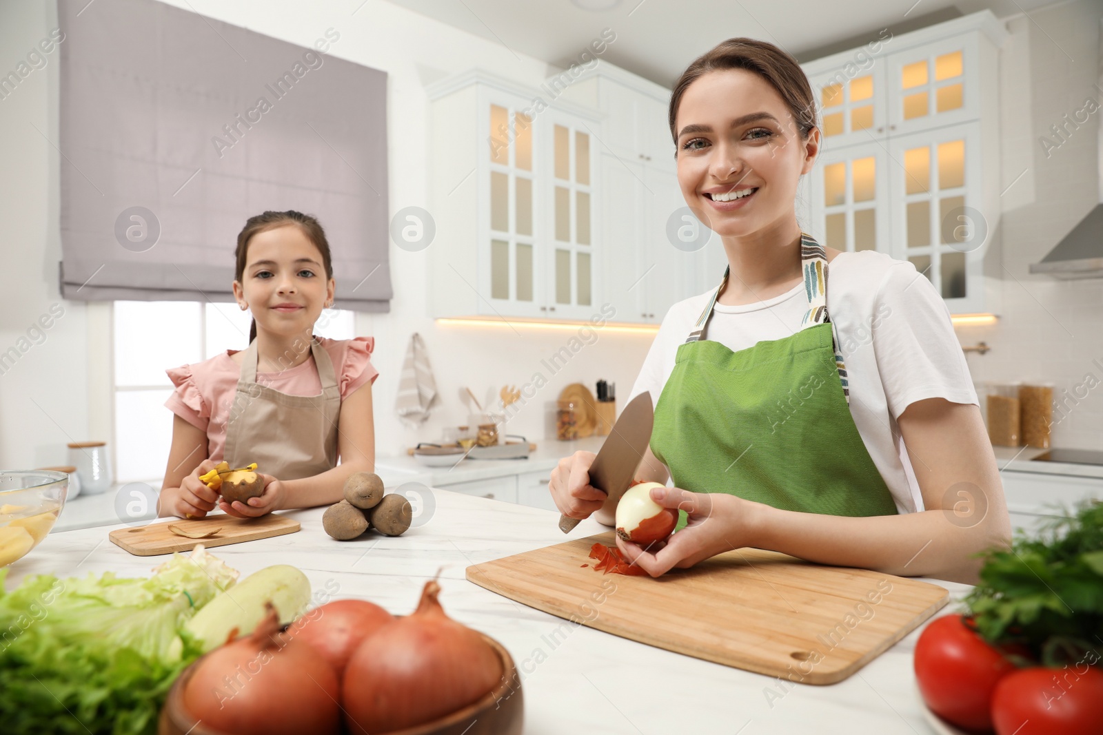 Photo of Mother and daughter peeling vegetables at table in kitchen