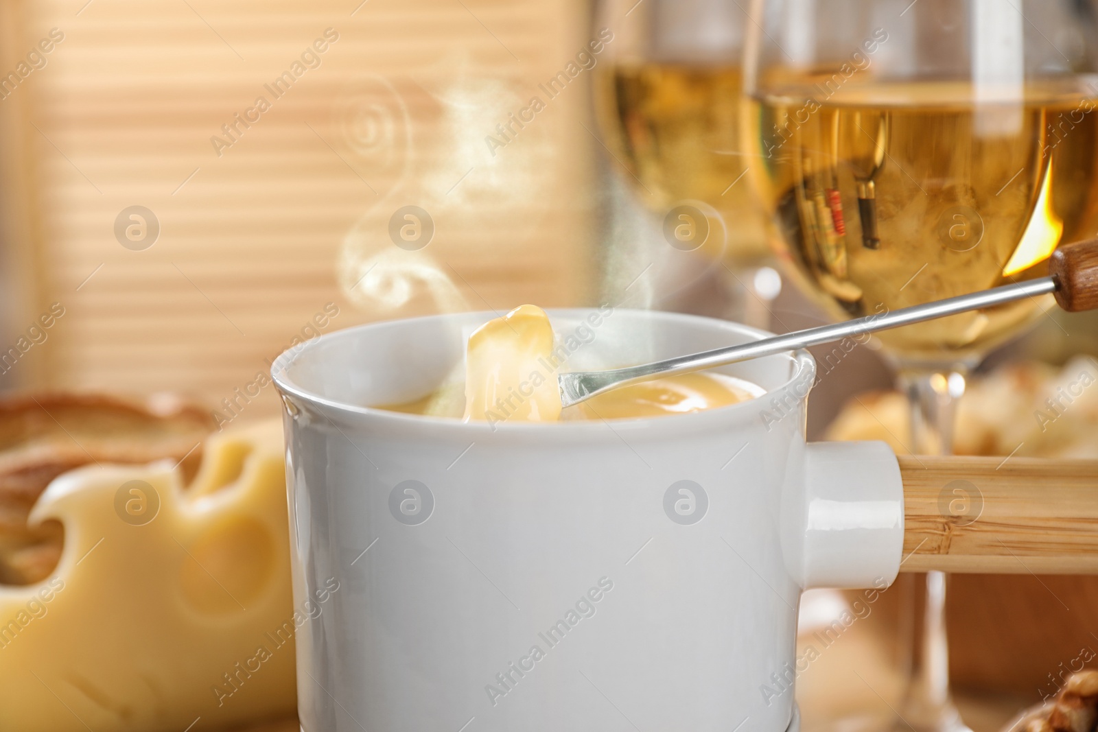 Image of Dipping piece of bread into fondue pot with tasty melted cheese at table, closeup