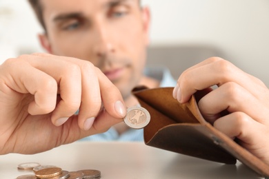 Man putting coins into wallet at table, focus on hands