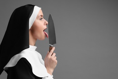 Photo of Woman in nun habit holding knife on grey background. Space for text