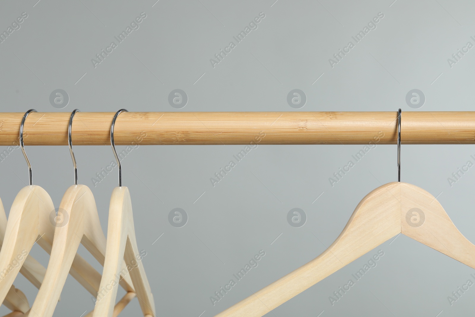 Photo of Empty clothes hangers on wooden rack against grey background, closeup