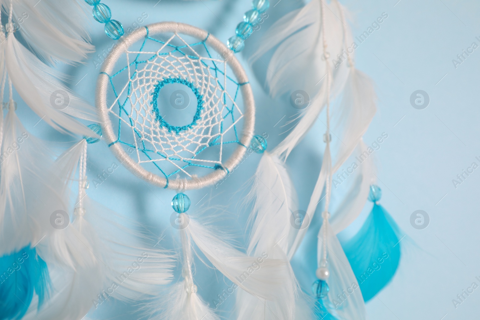 Photo of Beautiful dream catcher hanging on light blue background, closeup