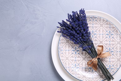 Photo of Bouquet of beautiful preserved lavender flowers and plates on light grey textured table, top view. Space for text