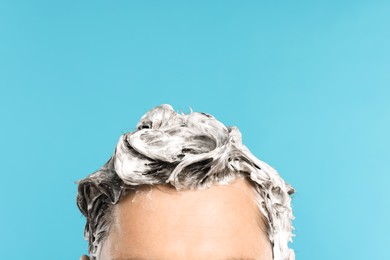Photo of Man with shampoo foam on his head against light blue background, closeup. Space for text