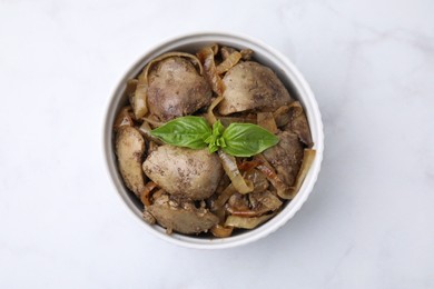 Delicious fried chicken liver with onion and basil in bowl on white marble table, top view