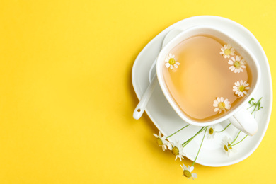 Delicious chamomile tea in cup on yellow background, top view. Space for text