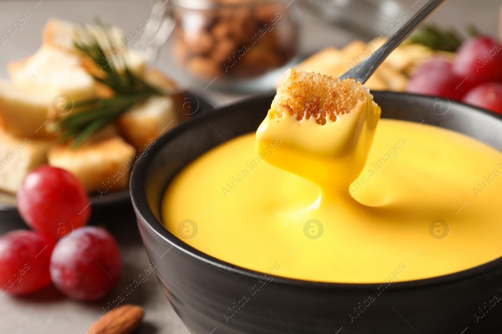 Photo of Dipping piece of bread into tasty cheese fondue at table, closeup