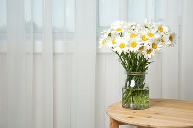 Vase with beautiful chamomile flowers on table