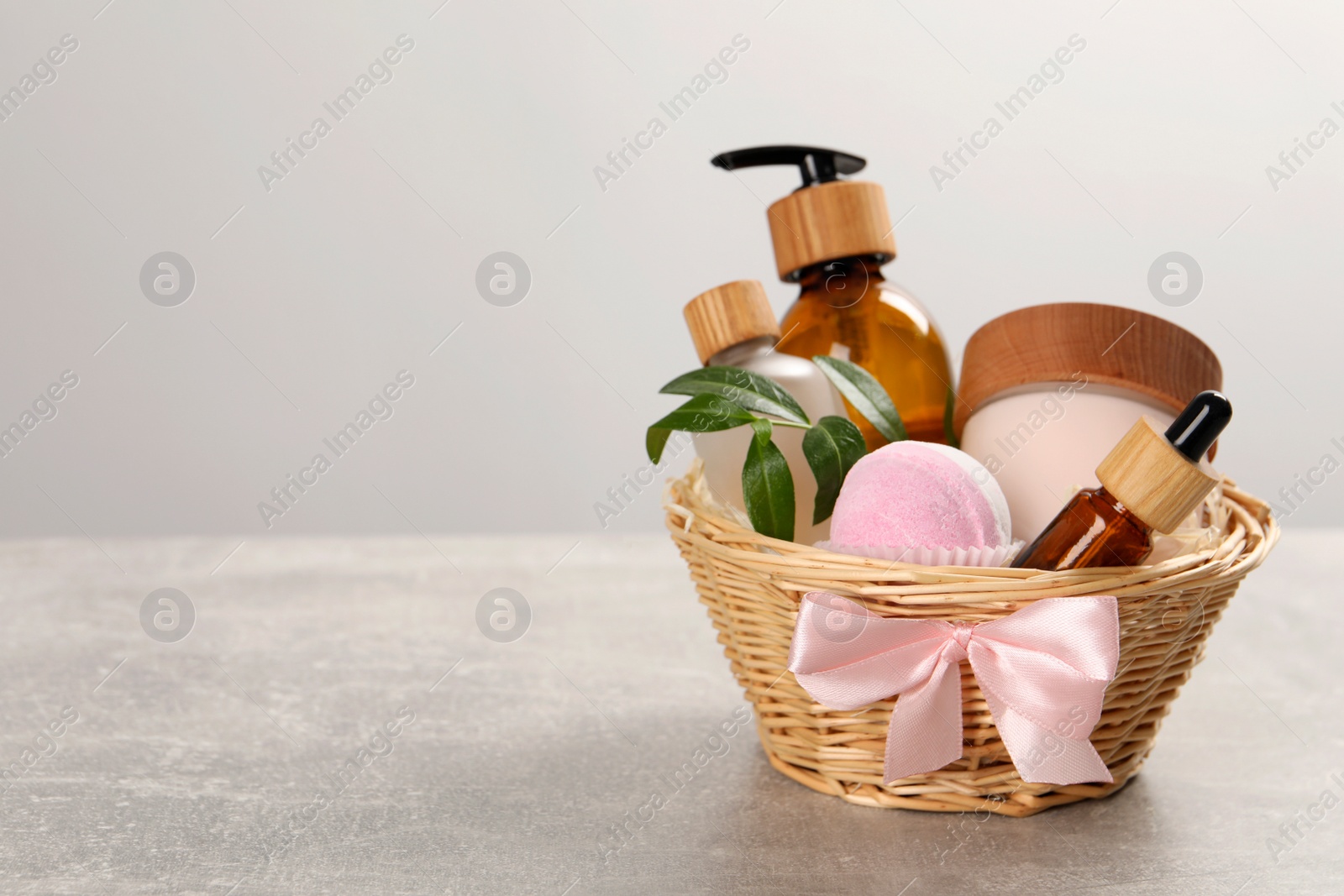 Photo of Spa gift set of different luxury products in wicker basket on grey table, space for text