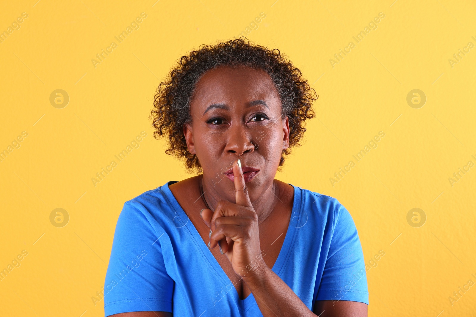 Photo of Portrait of African-American woman making silent gesture on yellow background